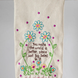 Decorative towel with floral embroidery and pom-pom trim on a wooden stick against a gray background