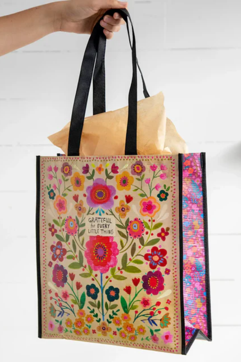 Floral-patterned tote bag with text held by a hand on a white background
