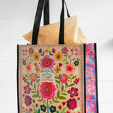 Floral-patterned tote bag with text held by a hand on a white background