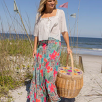 Woman on a beach holding a picnic basket, wearing a floral skirt and white top.