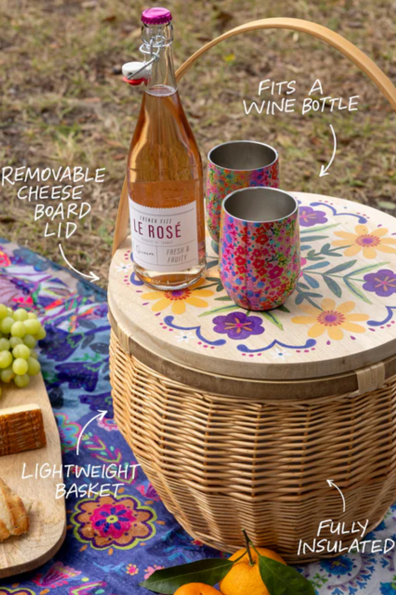 Picnic basket with a bottle of wine, cups, and snacks on a colorful tablecloth.