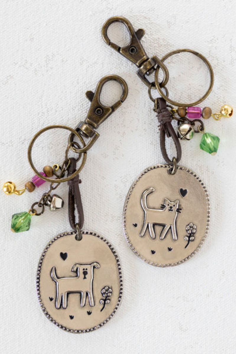 Two keychains with cat designs on oval pendants against a white background
