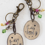 Two keychains with cat designs on oval pendants against a white background