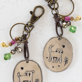 Two keychains with cat designs on oval pendants against a white background