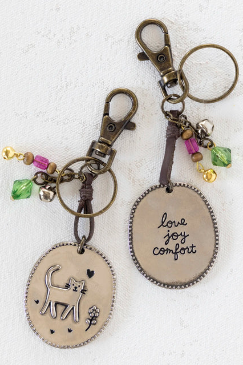 Two keychains with oval pendants featuring cat illustrations and engraved text on a white background.
