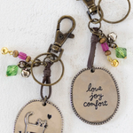 Two keychains with oval pendants featuring cat illustrations and engraved text on a white background.