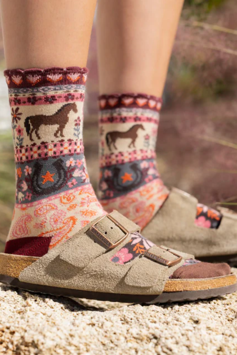 Person wearing patterned socks with horse design and sandals on a natural background