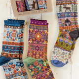 Colorful patterned socks displayed on a wooden stand with packaging in the background.