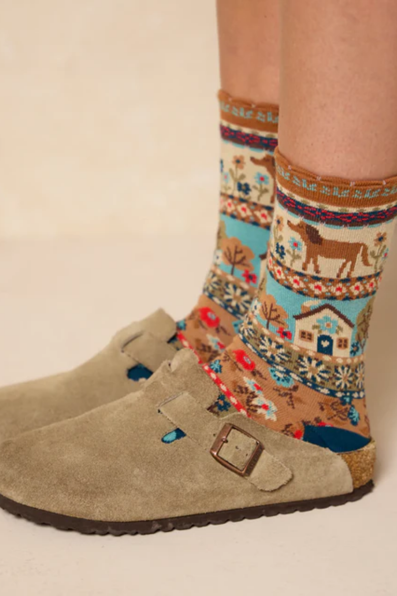 Patterned socks with a horse design worn with beige boots on a neutral background