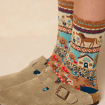 Patterned socks with a horse design worn with beige boots on a neutral background