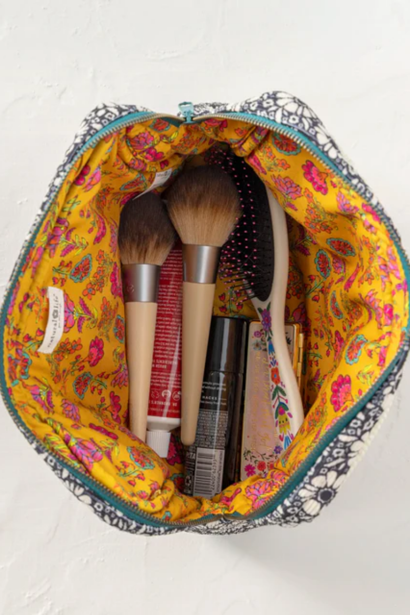 Makeup brushes and products in a colorful makeup bag on a white background