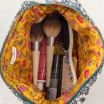 Makeup brushes and products in a colorful makeup bag on a white background