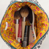 Makeup brushes and products in a colorful makeup bag on a white background