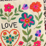 Embroidered fabric with flowers, a heart, and the word 'LOVE' on a colorful background.