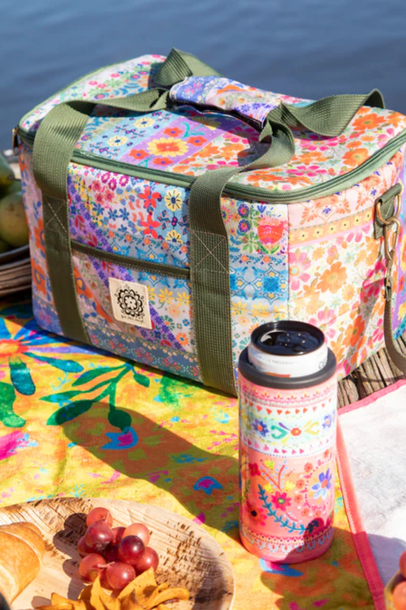 Colorful floral-patterned cooler bag with a thermos on a picnic setup by a body of water.