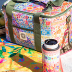Colorful floral-patterned cooler bag with a thermos on a picnic setup by a body of water.