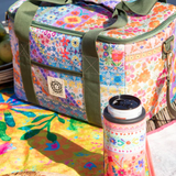 Colorful floral-patterned cooler bag with a thermos on a picnic setup by a body of water.