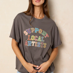 Woman wearing a gray t-shirt with 'Support Local Artists' text in colorful letters against a beige background