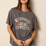 Woman wearing a gray t-shirt with 'Support Local Artists' text in colorful letters against a beige background