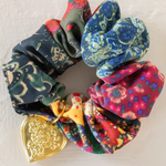 Colorful scrunchies with a gold heart-shaped charm on a light background