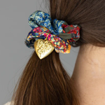 Floral scrunchie with a gold heart clip in a person's hair against a gray background