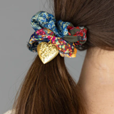 Floral scrunchie with a gold heart clip in a person's hair against a gray background