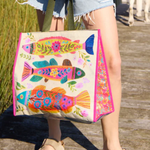Person holding a colorful fish-patterned bag on a wooden deck with grass in the background