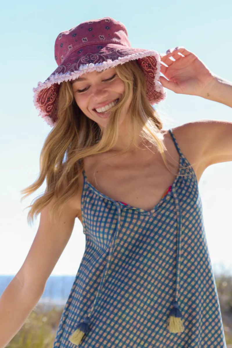 Woman wearing a red patterned hat and blue checkered dress outdoors.