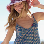 Woman wearing a red patterned hat and blue checkered dress outdoors.