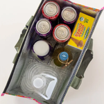 Assorted items including jars, a box of cookies, and a tumbler in a green bag on a white background