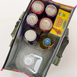 Assorted items including jars, a box of cookies, and a tumbler in a green bag on a white background