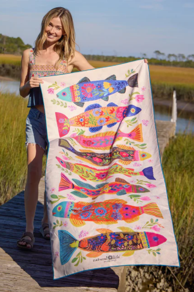 Woman holding a colorful fish-patterned towel by a body of water.