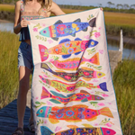 Woman holding a colorful fish-patterned towel by a body of water.
