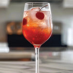 Glass of red cocktail with cherries on a marble countertop