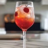 Glass of red cocktail with cherries on a marble countertop