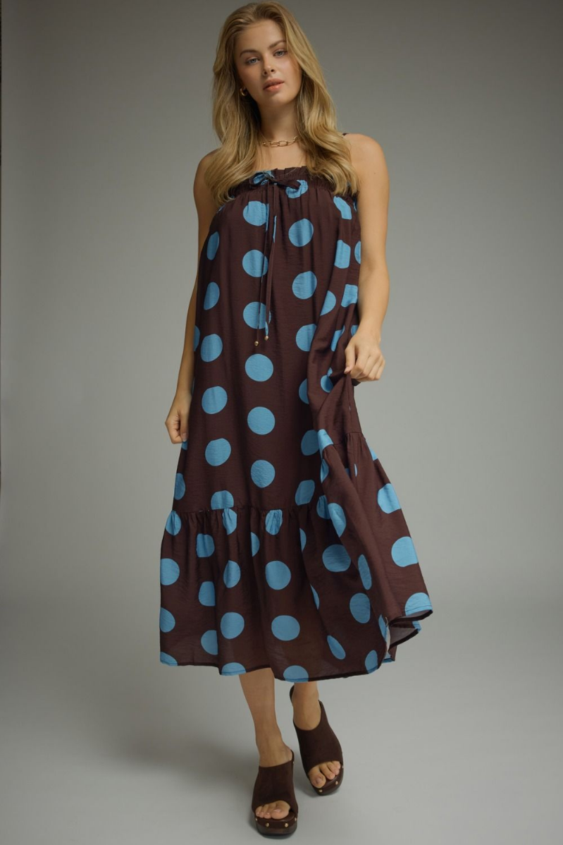 Woman wearing a brown dress with blue polka dots against a gray background