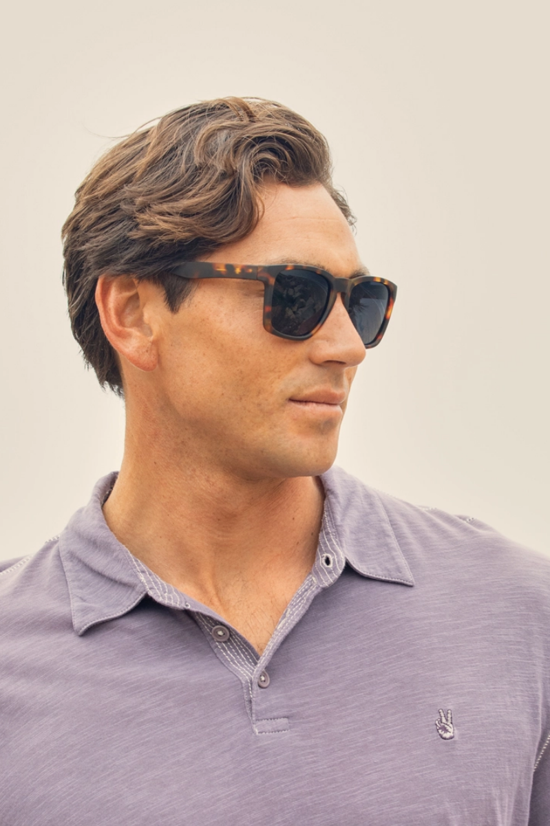 Man wearing sunglasses and a purple polo shirt against a neutral background