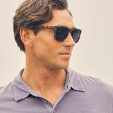 Man wearing sunglasses and a purple polo shirt against a neutral background