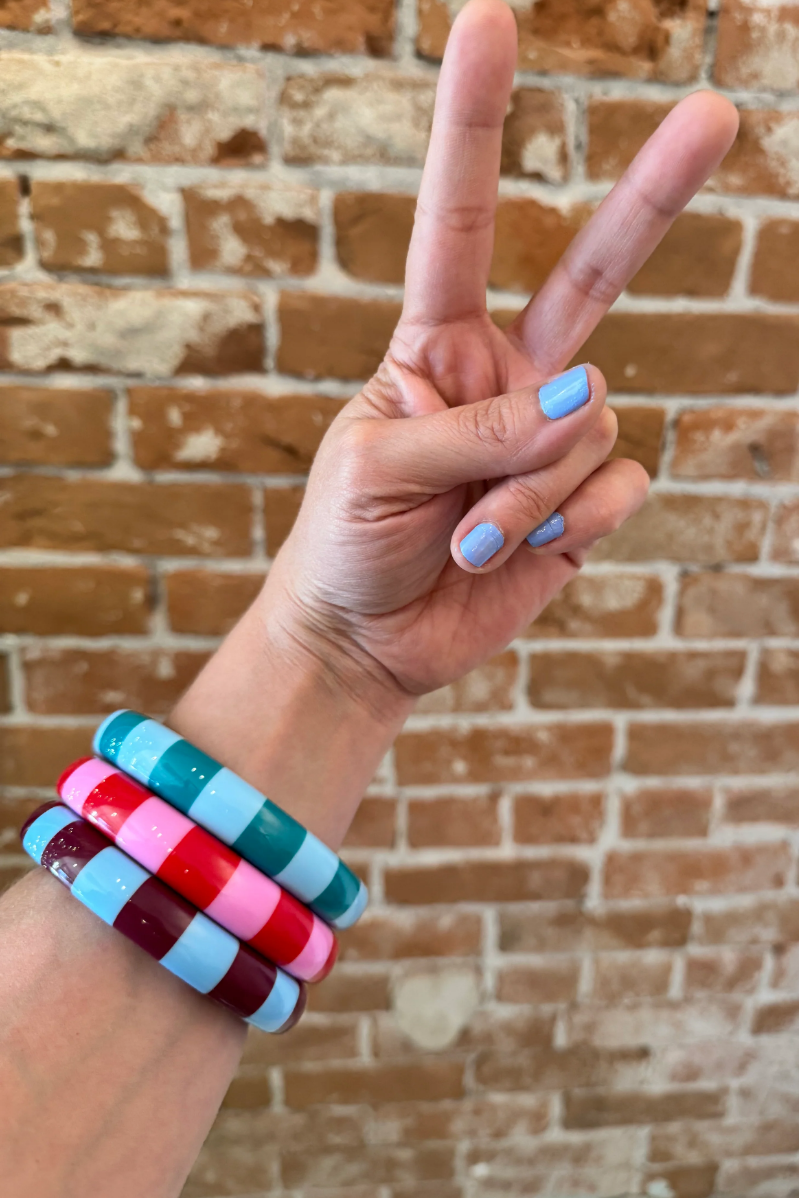 Woman wearing funky, chunky Color Crush Bangles in pink, green and brown, giving the peace sign against a brick wall. Super Groovy.