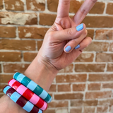 Woman wearing funky, chunky Color Crush Bangles in pink, green and brown, giving the peace sign against a brick wall. Super Groovy.