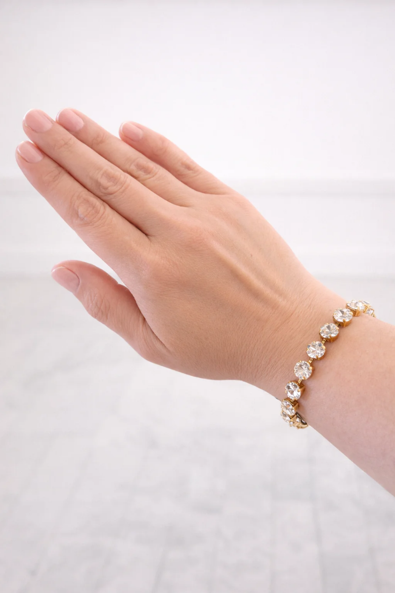 Hand wearing a gold bracelet with clear crystal stones on a white background