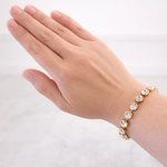 Hand wearing a gold bracelet with clear crystal stones on a white background