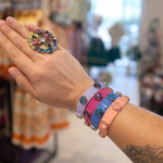 Hand wearing colorful bracelets with a ring, in a store setting