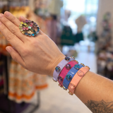 Hand wearing colorful bracelets with a ring, in a store setting