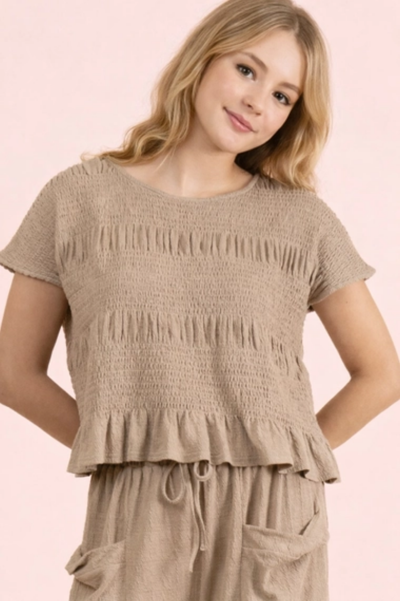 Young girl wearing a beige smocked top and pants on a pink background