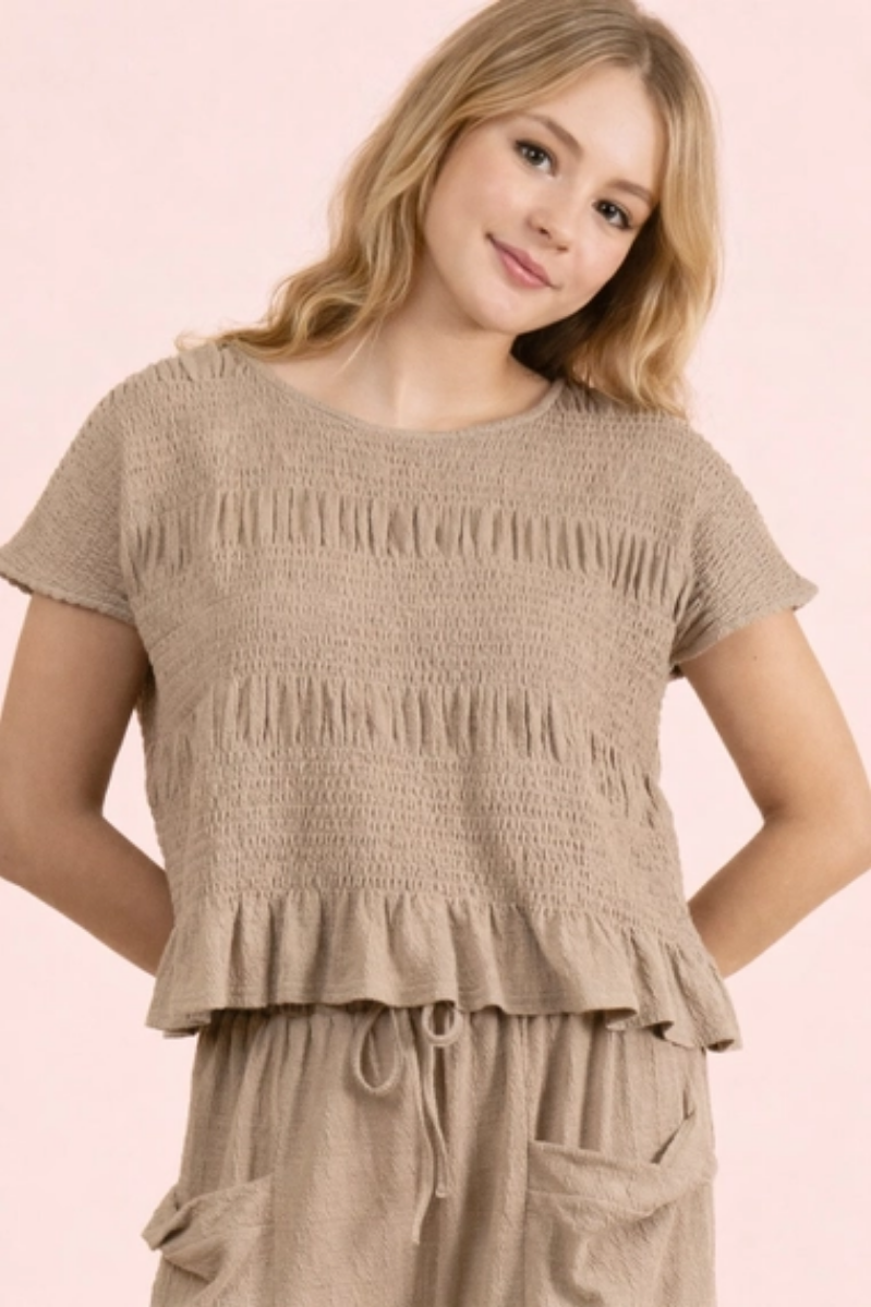 Young girl wearing a beige smocked top and pants on a pink background