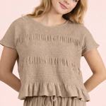Young girl wearing a beige smocked top and pants on a pink background