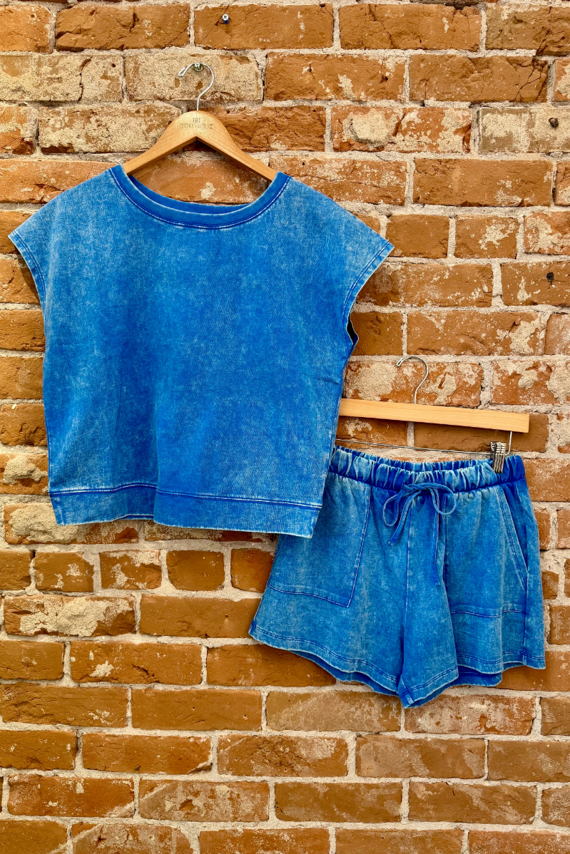Blue crop top and shorts set on a wooden hanger against a brick wall.