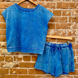 Blue crop top and shorts set on a wooden hanger against a brick wall.