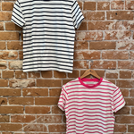 Two striped t-shirts hanging on wooden hangers against a brick wall.